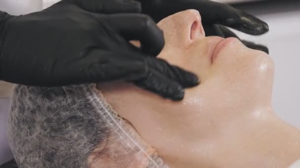 Косметична терапія. масаж обличчя. Косметологія догляд за шкірою. крупним планом. жінка отримує масаж обличчя медовий скраб, тонізовані м'язи і шкіру обличчя лімфатичний дренаж, в клініці краси. анти-старіння процедура — стокове відео