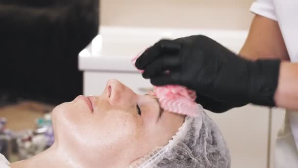 Beauty therapy. Cosmetology skin care. close-up. cosmetologist, in black medical gloves, removes remains of cosmetic face product, from female face with special wet wipes. anti aging procedure. Facial — Wideo stockowe