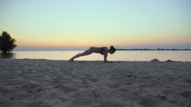 Açık havada uzanıyor. Yoga silueti. Yoga kumsalı. Atletik genç kadın gün batımında ya da gün doğumunda plajda yoga yapıyor. Spor salonu açık havada. Sabahları spor yapıyorum. Fitness, spor
