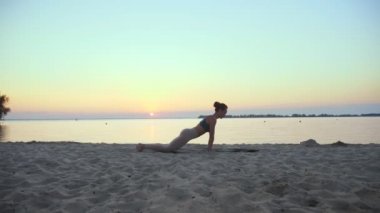 Açık havada uzanıyor. Yoga silueti. Yoga kumsalı. Atletik genç kadın gün batımında ya da gün doğumunda plajda yoga yapıyor. Spor salonu açık havada. Sabahları spor yapıyorum. Fitness, spor