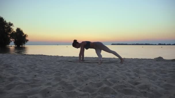 Açık havada uzanıyor. Yoga silueti. Yoga kumsalı. Atletik genç kadın gün batımında ya da gün doğumunda plajda yoga yapıyor. Spor salonu açık havada. Sabahları spor yapıyorum. Fitness, spor — Stok video