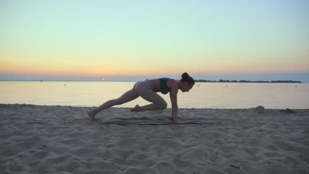 Açık havada uzanıyor. Yoga silueti. Yoga kumsalı. Atletik genç kadın gün batımında ya da gün doğumunda plajda yoga yapıyor. Spor salonu açık havada. Sabahları spor yapıyorum. Fitness, spor — Stok video