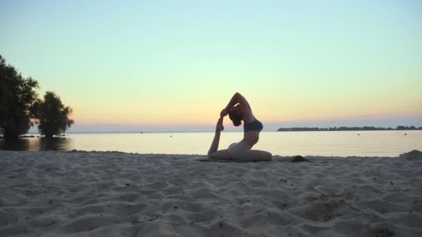 S'étirant à l'extérieur. silhouette de yoga. plage de yoga. La jeune femme sportive pratique le yoga à la plage au coucher du soleil ou au lever du soleil. Entraînement physique à l'extérieur. faire du sport le matin. Fitness, sport — Video