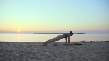 Açık havada uzanıyor. Yoga silueti. Yoga kumsalı. Atletik genç kadın gün batımında ya da gün doğumunda plajda yoga yapıyor. Spor salonu açık havada. Sabahları spor yapıyorum. Fitness, spor