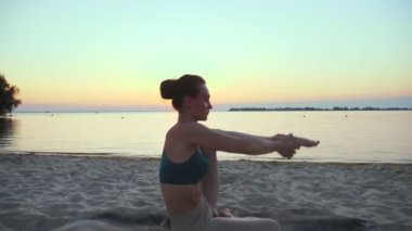 Açık havada uzanıyor. Yoga silueti. Yoga kumsalı. Atletik genç kadın gün batımında ya da gün doğumunda plajda yoga yapıyor. Spor salonu açık havada. Sabahları spor yapıyorum. Fitness, spor