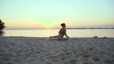 Açık havada uzanıyor. Yoga silueti. Yoga kumsalı. Atletik genç kadın gün batımında ya da gün doğumunda plajda yoga yapıyor. Spor salonu açık havada. Sabahları spor yapıyorum. Fitness, spor