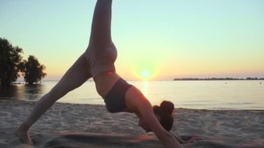 Açık havada uzanıyor. Yoga silueti. Yoga kumsalı. Atletik genç kadın gün batımında ya da gün doğumunda plajda yoga yapıyor. Spor salonu açık havada. Sabahları spor yapıyorum. Fitness, spor