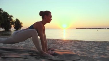 Açık havada uzanıyor. Yoga silueti. Yoga kumsalı. Atletik genç kadın gün batımında ya da gün doğumunda plajda yoga yapıyor. Spor salonu açık havada. Sabahları spor yapıyorum. Fitness, spor