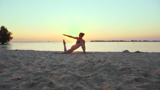 Rozciąga się na zewnątrz. sylwetka jogi. plaża jogi. Sportowa młoda kobieta ćwiczy jogę na plaży podczas zachodu lub wschodu słońca. Trening fitness na świeżym powietrzu. uprawianie sportu rano. Sprawność, sport — Wideo stockowe