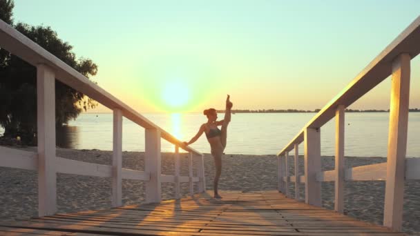 Barre. jak se natahují venku. Jóga pláž. baletní trénink. Atletická mladá žena cvičí na pláži během západu slunce nebo východu slunce. Fitness trénink venku. Fitness, balet, sport, jóga a — Stock video