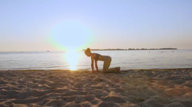 Bar antrenmanı. Açık havada uzanıyor. Yoga kumsalı. Atletik genç kadın gün batımında ya da gün doğumunda plajda minder üzerinde egzersiz yapıyor. Spor salonu açık havada. Fitness, bale, spor, yoga ve