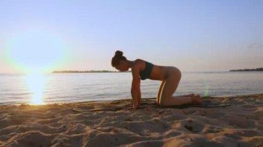 Bar antrenmanı. Açık havada uzanıyor. Yoga kumsalı. Atletik genç kadın gün batımında ya da gün doğumunda plajda minder üzerinde egzersiz yapıyor. Spor salonu açık havada. Fitness, bale, spor, yoga ve