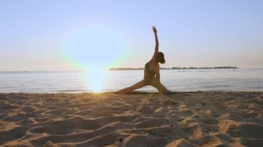 Bar antrenmanı. Açık havada uzanıyor. Yoga kumsalı. Atletik genç kadın gün batımında ya da gün doğumunda plajda minder üzerinde egzersiz yapıyor. Spor salonu açık havada. Fitness, bale, spor, yoga ve