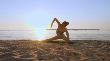 Bar antrenmanı. Açık havada uzanıyor. Yoga kumsalı. Atletik genç kadın gün batımında ya da gün doğumunda plajda minder üzerinde egzersiz yapıyor. Spor salonu açık havada. Fitness, bale, spor, yoga ve