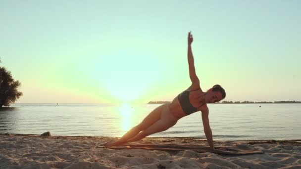 Entrenamiento de barra. estiramiento al aire libre. Playa de yoga. Mujer joven atlética está haciendo ejercicios en la estera, en la playa durante el atardecer o la salida del sol. Entrenamiento físico al aire libre. Fitness, ballet, deporte, yoga y — Vídeo de stock