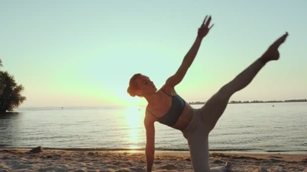 Exercițiu barre. Se întinde în aer liber. plaja yoga. O tânără atletică face exerciții pe covor, pe plajă în timpul apusului de soare sau răsăritul soarelui. Antrenament de fitness în aer liber. Fitness, balet, sport, yoga și — Videoclip de stoc