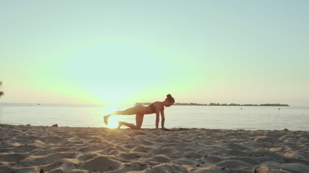 Bar antrenmanı. Açık havada uzanıyor. Yoga kumsalı. Atletik genç kadın gün batımında ya da gün doğumunda plajda minder üzerinde egzersiz yapıyor. Spor salonu açık havada. Fitness, bale, spor, yoga ve — Stok video