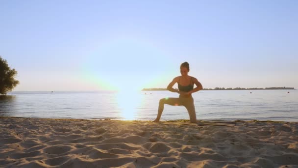 Entrenamiento de barra. estiramiento al aire libre. Playa de yoga. Mujer joven atlética está haciendo ejercicios en la estera, en la playa durante el atardecer o la salida del sol. Entrenamiento físico al aire libre. Fitness, ballet, deporte, yoga y — Vídeo de stock