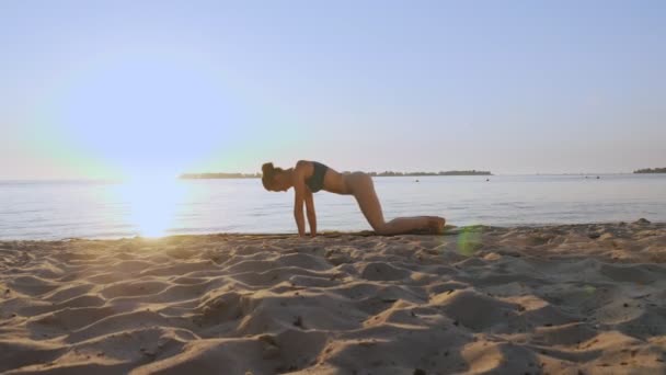 Bares Training. Dehnen im Freien. Yoga-Strand. Sportliche junge Frau macht Übungen auf Matten, am Strand bei Sonnenuntergang oder Sonnenaufgang. Fitnesstraining im Freien. Fitness, Ballett, Sport, Yoga und — Stockvideo