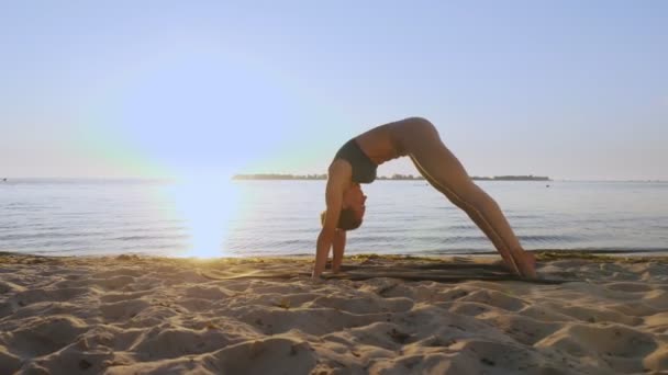 Bar antrenmanı. Açık havada uzanıyor. Yoga kumsalı. Atletik genç kadın gün batımında ya da gün doğumunda plajda minder üzerinde egzersiz yapıyor. Spor salonu açık havada. Fitness, bale, spor, yoga ve — Stok video