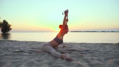 Açık havada uzanıyor. Fitness elastik bant. Atletik genç kadın gün batımında veya gün doğumunda plajda spor yaparken elastik bant kullanıyor. Spor salonu açık havada. Spor yaparken.