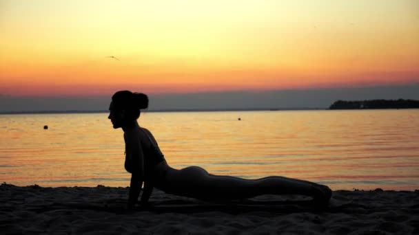 Yoga-Silhouette. Dehnen im Freien. Yoga-Strand. Die Silhouette einer Frau praktiziert Yoga am Strand bei Sonnenuntergang oder Sonnenaufgang. Fitnesstraining im Freien. Sport treiben am Morgen. Fitness, sport — Stockvideo