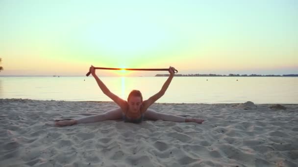 Uitrekken buiten. fitness elastiek. Atletische jonge vrouw doet oefeningen met behulp van fitness elastische band, op het strand tijdens zonsondergang of zonsopgang. Fitness training buiten. sporten in de — Stockvideo