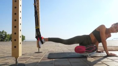 Açık havada egzersiz. Askı kayışları. Kayışlarla egzersiz yap. Atletik genç kadın gün batımında ya da gün doğumunda plajda halatlı halatlar kullanarak tüm vücut direnci egzersizleri yapıyor. Fitness eğitimi