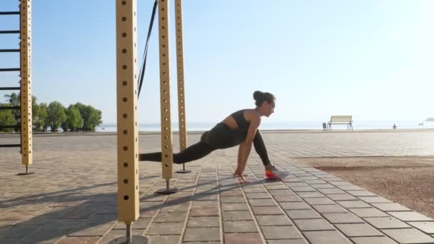 Trening na świeżym powietrzu. paski zawieszenia. trening z paskami. Sportowa młoda kobieta wykonuje ćwiczenia opór całego ciała za pomocą pętli liny TRX, na plaży podczas zachodu lub wschodu słońca. Trening fitness — Wideo stockowe