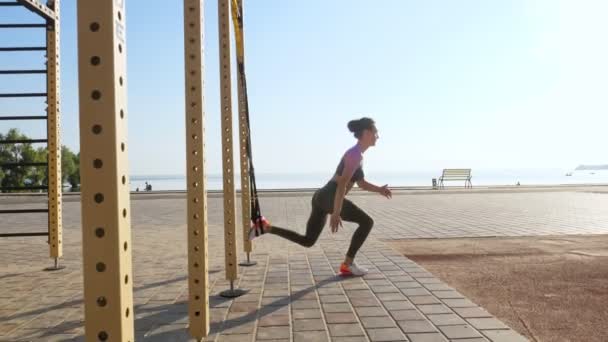 Hacer ejercicio al aire libre. correas de suspensión. entrenamiento con correas. Mujer joven atlética está haciendo ejercicios de resistencia todo el cuerpo utilizando cuerdas enroscadas TRX, en la playa durante el atardecer o la salida del sol. Entrenamiento de fitness — Vídeo de stock