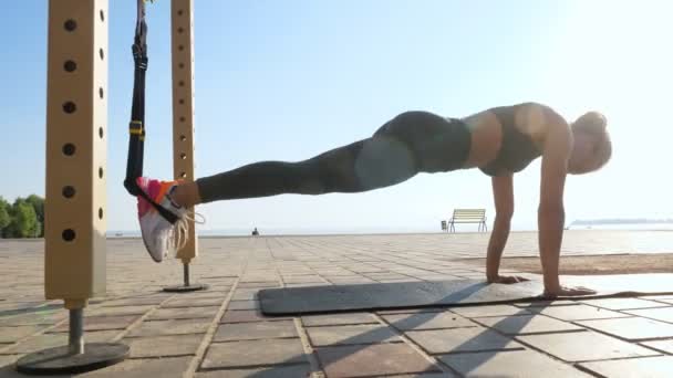 Trening na świeżym powietrzu. paski zawieszenia. trening z paskami. Sportowa młoda kobieta wykonuje ćwiczenia opór całego ciała za pomocą pętli liny TRX, na plaży podczas zachodu lub wschodu słońca. Trening fitness — Wideo stockowe