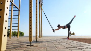 Açık havada egzersiz. Askı kayışları. Kayışlarla egzersiz yap. Atletik genç kadın gün batımında ya da gün doğumunda plajda halatlı halatlar kullanarak tüm vücut direnci egzersizleri yapıyor. Fitness eğitimi