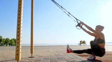 Açık havada egzersiz. Askı kayışları. Kayışlarla egzersiz yap. Atletik genç kadın gün batımında ya da gün doğumunda plajda halatlı halatlar kullanarak tüm vücut direnci egzersizleri yapıyor. Fitness eğitimi