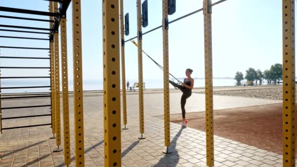 Trening na świeżym powietrzu. paski zawieszenia. trening z paskami. Sportowa młoda kobieta wykonuje ćwiczenia opór całego ciała za pomocą pętli liny TRX, na plaży podczas zachodu lub wschodu słońca. Trening fitness — Wideo stockowe