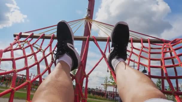 Pies en hamaca. piernas en una hamaca. Primer plano. un hombre, en zapatillas negras, está descansando en una hamaca, sobre el fondo del cielo azul. Vista en primera persona — Vídeos de Stock