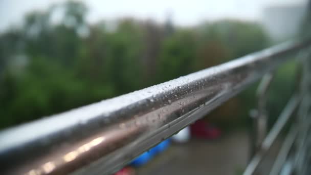 Lluvia. Llueve. Primer plano. gotas de lluvia gotean sobre la superficie brillante de la barandilla metálica del balcón y fluyen hacia abajo, durante la lluvia. verano día lluvioso. — Vídeo de stock