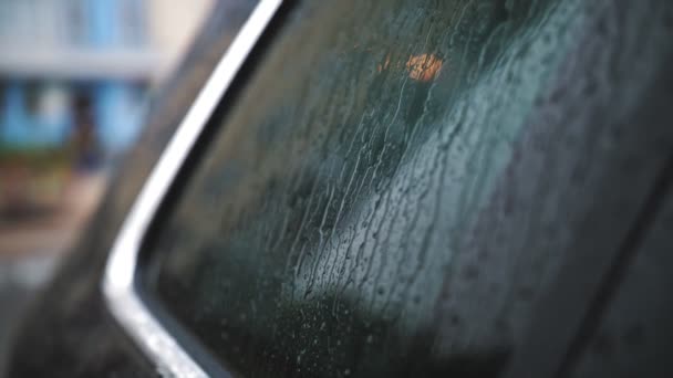 Gotas de lluvia en el coche. Lluvia. Llueve. gotas de lluvia gotean y gotean lentamente, fluyendo por la superficie de cristal de la ventana del coche negro moderno, durante la lluvia. primer plano — Vídeos de Stock