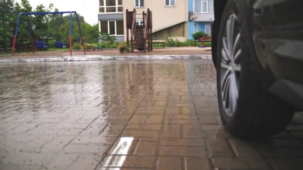 雨だ。接近中だ。雨滴は遊び場を背景にぬれた通りのタイルに落ちます。住宅街の中庭で雨が降っています。夏のシャワー. — ストック動画