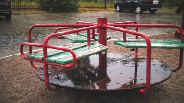 Raining on playground. close-up. Wet, empty merry go round carousel , in the yard, during heavy rain. — Stock Video