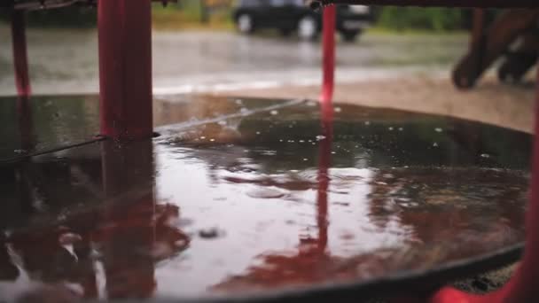 Raining on playground. close-up. raindrops fall into puddles, on wet, empty merry go round carousel , with splashes and bubbles. Empty playground in the yard, during heavy rain. — Stock Video