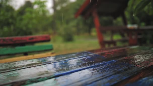 Rain, puddles. raining in the park. close-up. raindrops fall on wooden table, bench, gazebo with splashes and bubbles, during heavy rain, in empty park. summer rainy day. — Stock Video