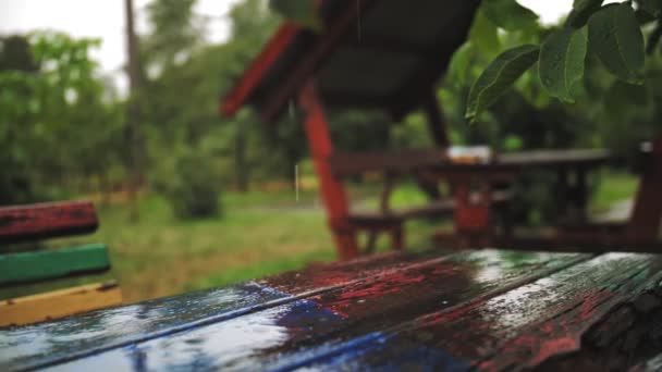 雨，水坑。在公园里下雨。特写。雨滴落在木制桌子、长椅、带着飞溅和气泡的凉亭上，下大雨时，空旷的公园里。夏季雨天. — 图库视频影像