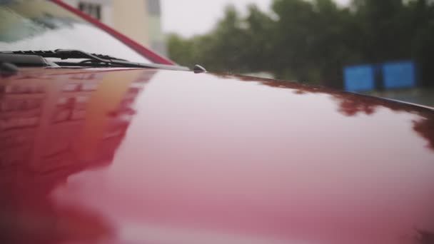 Gotas de lluvia en el coche. Lluvia. Llueve. gotas de lluvia caen con salpicaduras a la superficie del coche rojo moderno, durante las fuertes lluvias. primer plano — Vídeos de Stock