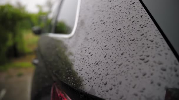 車の雨滴だ。雨だ。雨だ。雨滴は現代の黒い車の表面に落ち、ゆっくりと流れ落ち、雨の間に流れ落ちる。閉鎖 — ストック動画