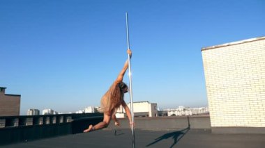 Direk dansı. uygun kadın jimnastikçi, bej mayosuyla, akrobatik egzersizler yapıyor metal döner direkte, gökdelen çatısında, muhteşem bir gündoğumu görüşü arka planında