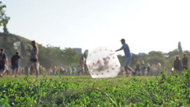 zorbing. Zorb topu. Şişme top. İnsanlar eğleniyor. Adam mutlu çocuğu çimlerin üzerinde, parkta, festival sırasında, şehir tatilinde, katranlı şişme topun içinde yuvarlıyor. yaz günü.