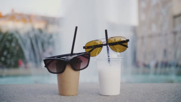 Kaffe att ta med. milkshake. Dricker att ta med. Ta med dig den. närbild. Två engångskoppar med kaffe och milkshake. solglasögon. stad fontän bakgrund. sommar — Stockvideo