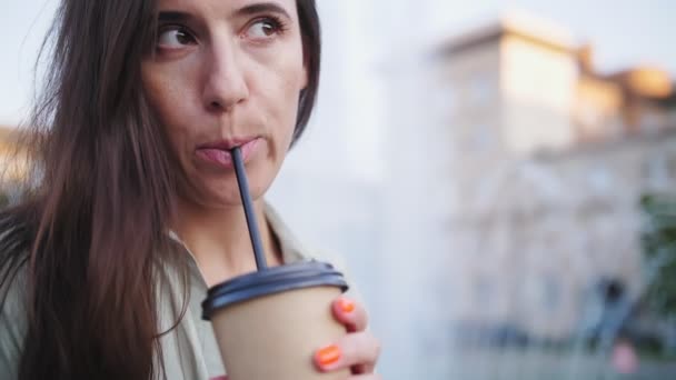 Café para levar. Café. latte. Bebida de café. uma jovem bebe através de uma palha seu latte de um copo de papel descartável, sentado junto a uma fonte, em uma noite de verão. — Vídeo de Stock