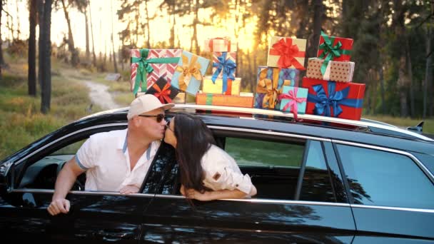 車のギフトボックス。新婚旅行だ。愛のカップル車の中でキス多くの美しい包装された小包、車の屋根の箱、太陽の下で、日没時に。配達だ。オンライン注文。記念日プレゼント — ストック動画