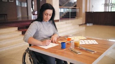 Tekerlekli. Maluliyet. Engelli genç kadın resim çiziyor, tekerlekli sandalyede oturuyor. Engelliler için yaratıcı dersler. Eğitim, ilişki ve insanlık kavramı